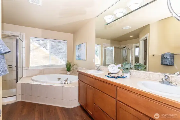 Elegant 5-piece ensuite bath featuring dual sinks, a large soaking tub, and a separate glass shower. Tile counters and flooring complement soft neutral tones, creating a serene spa-like space. Generous layout provides both functionality and relaxation.