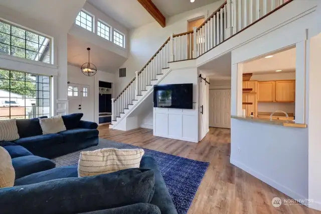 The great room with vaulted ceilings. Looking towards the main entrance and stairway to the 2nd floor. The hallway goes to the primary suite, down stairs half bath, utility room and garage. Lots of sunlight with this southern exposure.