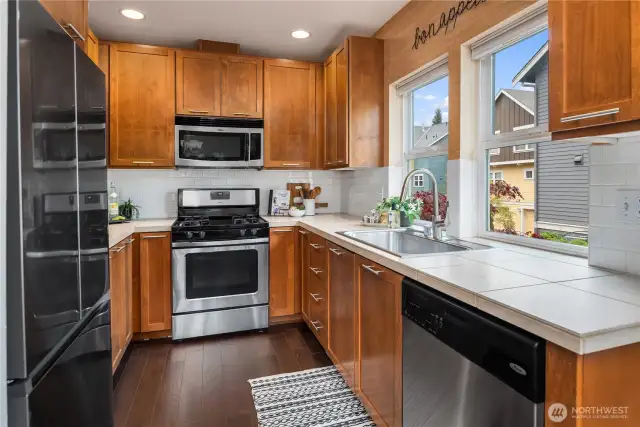 This thoughtful kitchen features wood cabinets and tile counters with a gas range.