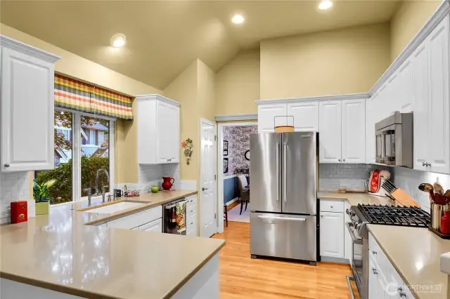 Remodeled kitchen. White, paneled cabinets. Plate rail in breakfast area. Grocery pantry with paneled Quaker door, ventilated wire shelving. Silestone® countertops, deep Limoges sink with English faucet, with west facing window and two-inch blinds, ISE® disposer. Silestone® breakfast bar. Counter-to-cabinet subway-tiled backsplash. KitchenAid® stainless French door refrigerator-freezer. KitchenAid® stainless dishwasher. KitchenAid® stainless duel-fuel gas range with electric oven. KitchenAid® stainless built-in microwave oven. Dramatic 12-foot-high coffered ceiling. Oak-hardwood floor.