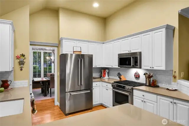 Remodeled kitchen. White, paneled cabinets. Plate rail in breakfast area. Grocery pantry with paneled Quaker door, ventilated wire shelving. Silestone® countertops, deep Limoges sink with English faucet, with west facing window and two-inch blinds, ISE® disposer. Silestone® breakfast bar. Counter-to-cabinet subway-tiled backsplash. KitchenAid® stainless French door refrigerator-freezer. KitchenAid® stainless dishwasher. KitchenAid® stainless duel-fuel gas range with electric oven. KitchenAid® stainless built-in microwave oven. Dramatic 12-foot-high coffered ceiling. Oak-hardwood floor.