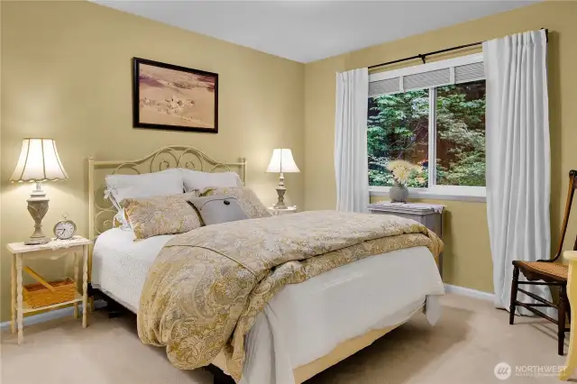 East bedroom. Paneled Quaker door. Neutral carpet. Closet with paneled bi-fold Quaker doors. Window with two-inch blinds and screen looking out to the woods behind.