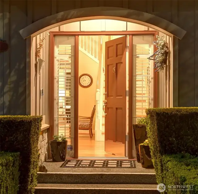 Arched, covered entry with timeless board and batten siding. Paneled Quaker door flanked by divided-light sidelight windows and two-inch Plantation-style shutters. Brushed nickel thumb latch door handle, security deadbolt lock, kickplate, door knocker on exterior.