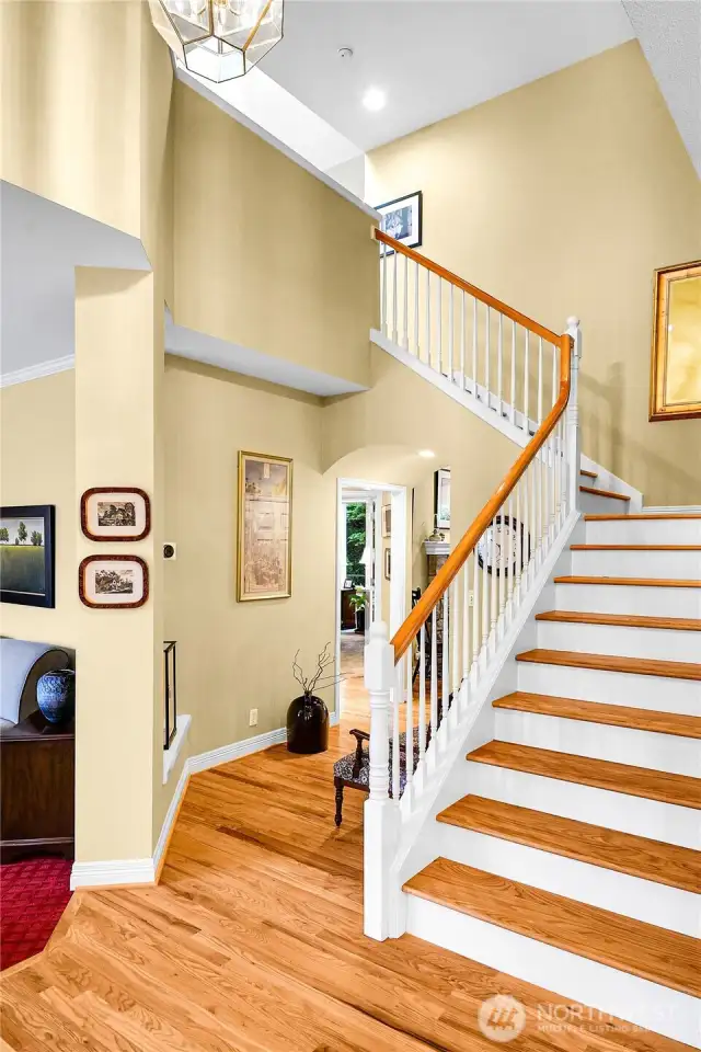 Entry interior. Dramatic, soaring ceiling with Traditional-style polished-brass-beveled-glass entry chandelier. Beautiful oak-hardwood floor. Elegant, atypical staircase with Traditional balustrade, oak-hardwood treads, formal painted risers. Hallway with archway opening and barrel-ceiling passageway to Family room. Entry coat closet with paneled door. Oak-hardwood floor extends into dining room, family room and hallway to Primary ensuite.