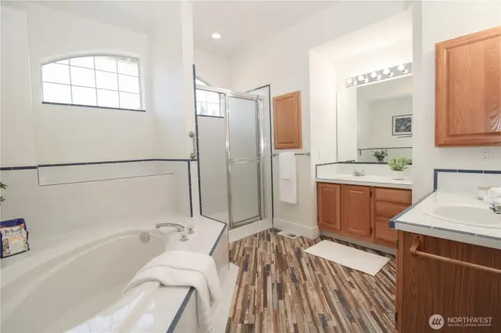 Luxurious 5-piece master suite bathroom boasts a soaking tub, separate shower, dual vanities, and beautiful tile flooring with decorative blue accent trim.