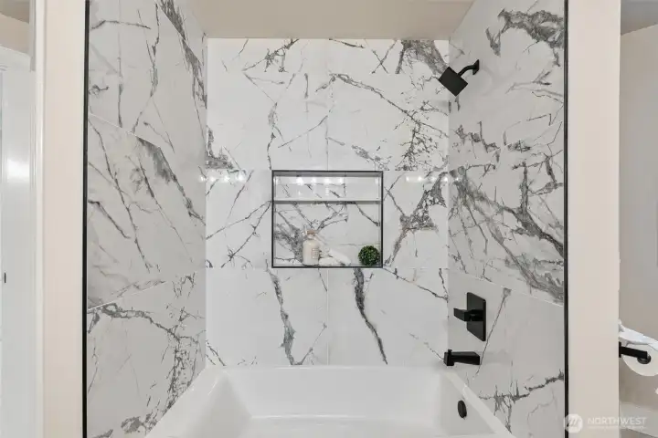 Full bath with marble-style surround and niche shelving detail.