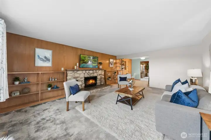 Expansive living room showcases a limestone marbel fireplace that anchors the space with natural texture and warmth. Built-in shelving along the wood-paneled wall provides display space and added functionality.