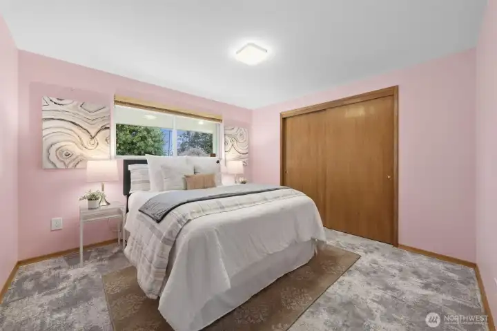 Bedroom One features soft natural light and a large updated vinyl window overlooking the yard. Plush carpeting adds comfort today, with hardwood floors preserved underneath for future options.