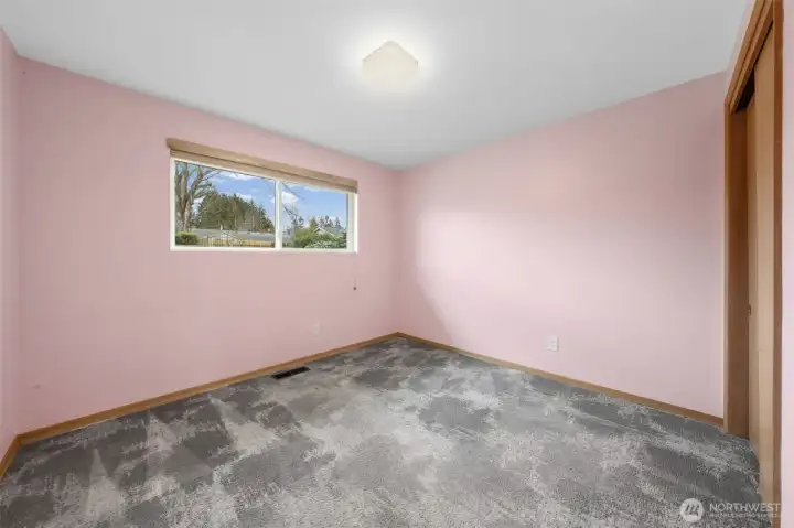 Bedroom Three featuring a wide updated vinyl window that frames neighborhood views and fills the space with natural light. The room is currently carpeted, with hardwood flooring located beneath.