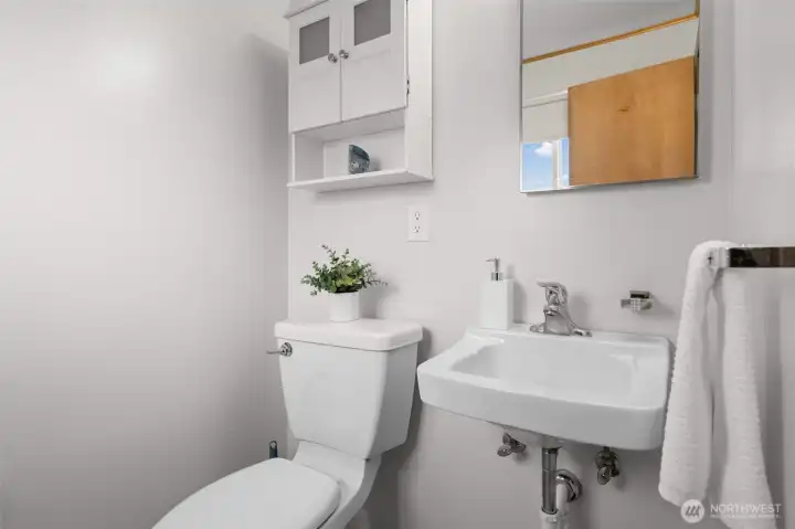 Convenient powder bath in the rec room with sink, mirror, and wall-mounted storage cabinet for essentials. Clean, simple layout makes it a practical addition for guests and everyday use.
