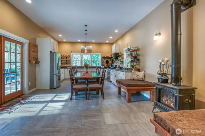 A spacious, light-filled kitchen perfect for entertaining—featuring granite countertops, radiant tile floors, abundant storage, built-in seating, a walk-in pantry, 5-burner gas range, freestanding propane fireplace, and a recently upgraded mini-split heater for comfort and efficiency.