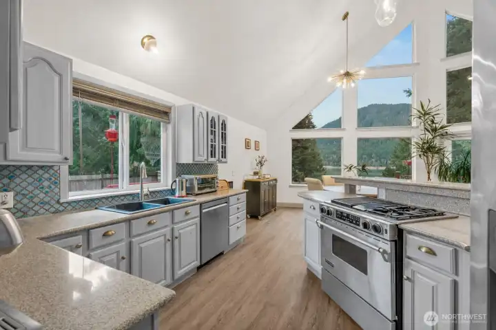 Open-concept layout with vaulted ceilings and abundant light flooding through the dramatic floor-to-ceiling windows overlooking the lake. This updated kitchen is equipped with modern stainless appliances including gas stove/range situated where you can cook with a view.