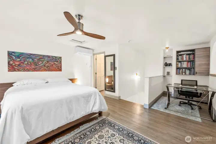 Primary bedroom with mini-split located next to bathroom entrance on left, stairway in the middle and nook on the right with extra built-ins for storage use, and a peak-a-boo view of the lake.