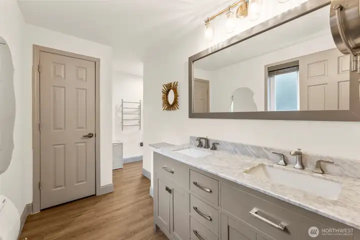 Primary suite bathroom vanity with dual inset  sinks and large horizontal mirror. Around the corner is towel rack, shower/tub and linen  closet space. Behind closed door houses the  toilet for extra privacy.
