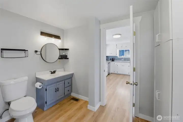 Updated full bath — Clean, modern bathroom with a round mirror, vanity, and a peek-through to the kitchen.