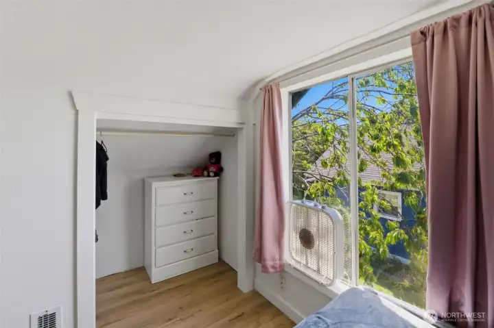 Smart storage — Built-in closet nook with dresser space and a window framing leafy treetop views.