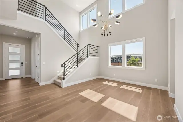 Striking entryway with modern staircase, statement chandelier, and double-height ceilings—flooded with natural light.