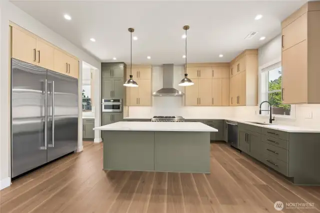 Beautifully designed kitchen with a warm yet modern aesthetic, showcasing a stylish two-tone palette of sage green and light wood cabinetry. Features include quartz countertops, a full-height tile backsplash, stainless steel appliances, and a large central island illuminated by statement pendant lighting.
