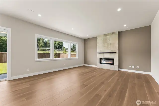 Modern open-concept living room featuring wide-plank hardwood floors, large energy-efficient windows, and a contemporary tile fireplace—perfect for natural light and indoor-outdoor living.