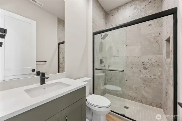 Modern guest bathroom featuring a quartz countertop, sleek matte black fixtures, and a full tile walk-in shower with glass enclosure.