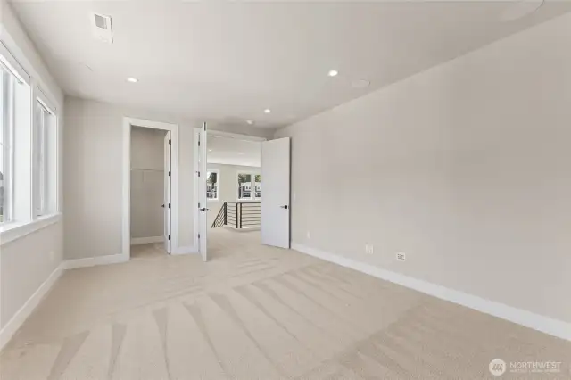 Bright upstairs bedroom with walk-in closet, plush carpet, and an open feel overlooking the loft.
