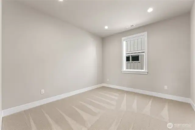 Spacious secondary bedroom with neutral tones, plush carpet, and recessed lighting.