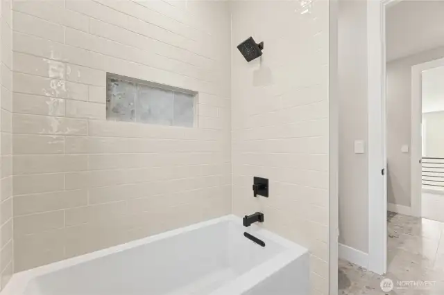Modern tub/shower combo with full-height tile surround, matte black fixtures, and built-in niche for storage.