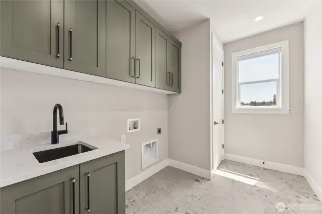 Stylish laundry room featuring sage cabinetry, quartz countertops, a built-in utility sink, and abundant natural light from a well-placed window.