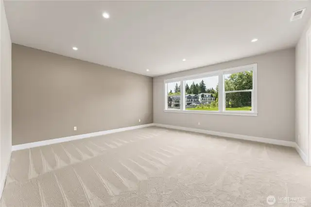 Expansive primary suite with plush carpet, soft accent wall, and oversized windows offering serene greenbelt views.