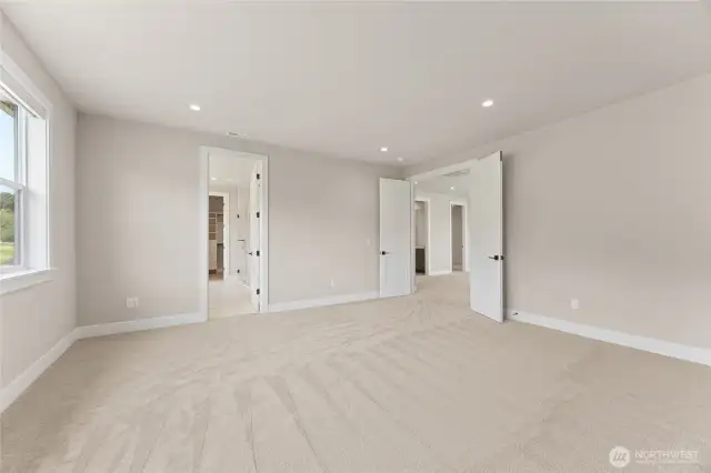 Spacious primary suite with plush carpet, recessed lighting, and a walk-in closet plus en suite bath access through elegant double doors.