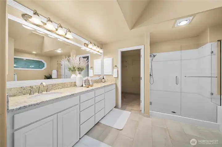 Spa-like primary bath showcasing an extended double vanity with granite countertops, a glass-enclosed walk-in shower, and direct access to a generous walk-in closet
