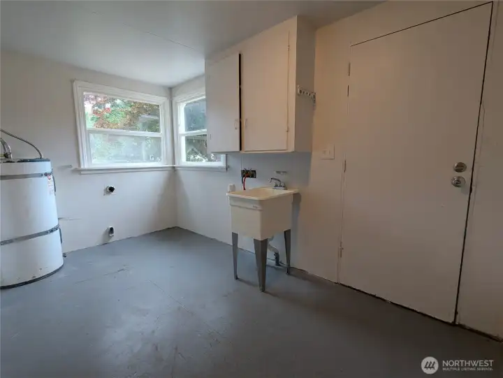 Large utility room with washer and dryer hookups next to the sink. There is a half bathroom next to this room. The door in the picture goes to the backyard.