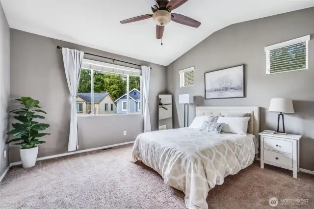 Retreat to the spacious and serene primary suite, featuring tall vaulted ceilings, a stylish ceiling fan, plush carpeting, and large windows that fill the room with natural light. Thoughtfully designed with comfort in mind, this inviting space offers the perfect place to unwind and recharge.