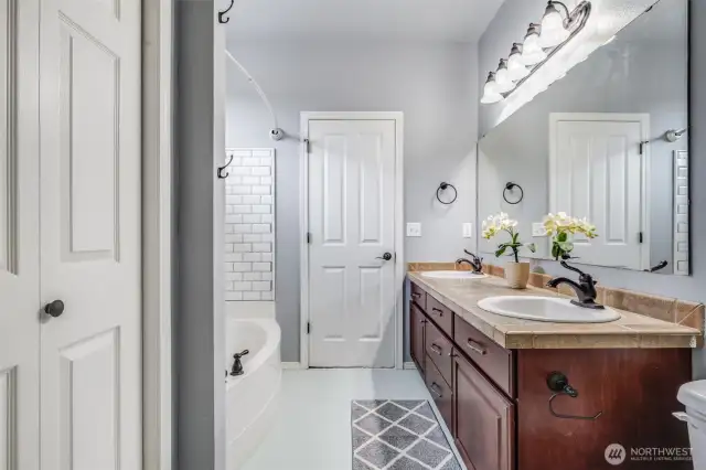 The primary bathroom offers a blend of style and functionality with tile flooring, dual vanities, a spacious shower-tub combo, and a convenient linen closet for added storage.