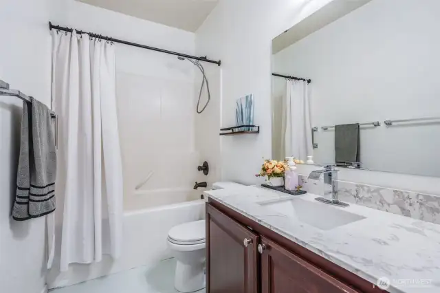 The stylish hall bathroom features a sleek quartz vanity, durable tile flooring, and a convenient shower-tub combo, offering both functionality and modern charm.