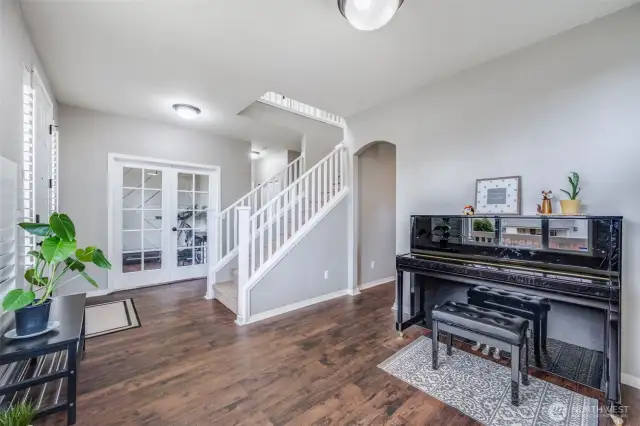 This versatile front room, currently used as a music space, features rich laminate wood flooring, elegant plantation shutters, and an open layout—perfect for a formal dining room or a cozy sitting area.