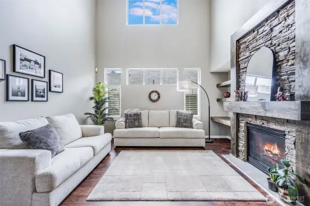 Soaring vaulted ceilings and abundant natural light create an airy ambiance in this stunning living room, featuring a unique stone-accented gas fireplace with floating wood shelves.