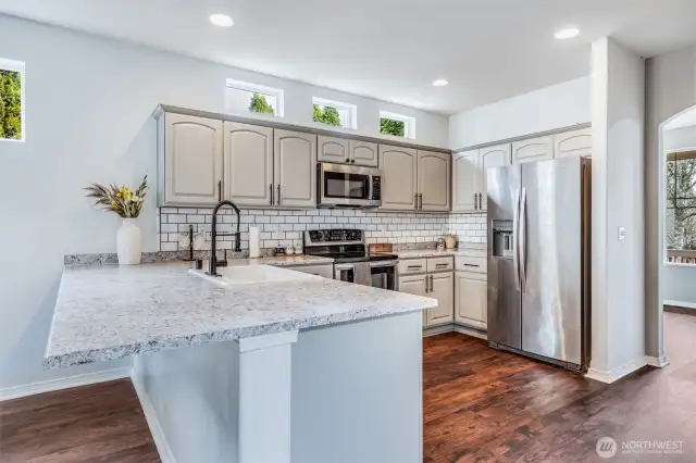 This stylish kitchen features beautiful cabinetry, a spacious breakfast bar for casual seating, and high-set windows that bring in abundant natural light, creating a bright and inviting space for cooking and gathering.