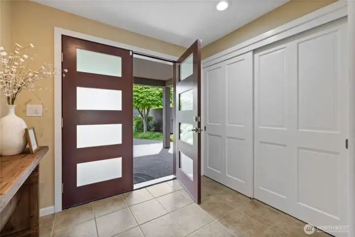 Striking modern double-door entry opens to a bright, welcoming foyer with tile flooring, generous storage, and a seamless connection to the private, landscaped courtyard.