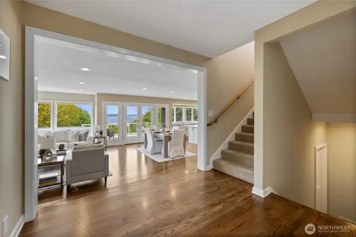 Grand entry transitions into an expansive, light-filled great room with rich hardwood floors, open sightlines, and immediate connection to view-filled living and dining spaces; staircase access thoughtfully positioned for functional flow.