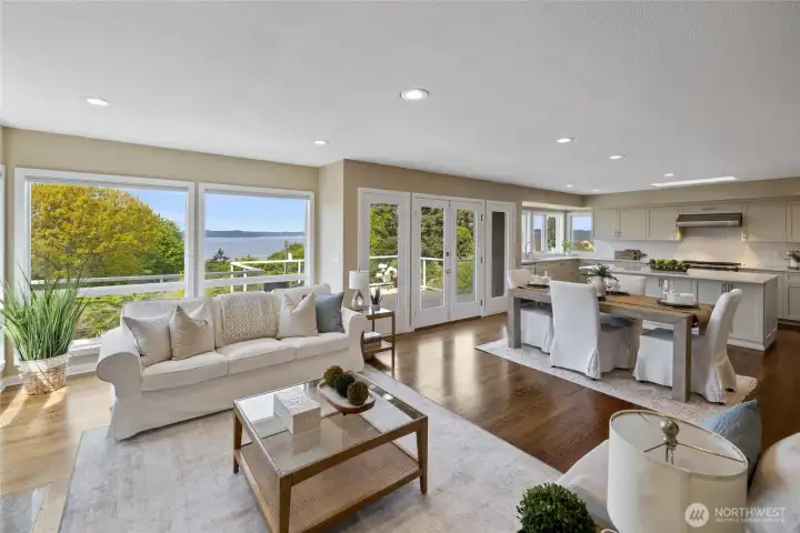 Light-filled living room with expansive windows capturing stunning water views, cozy fireplace, and seamless access to view deck.