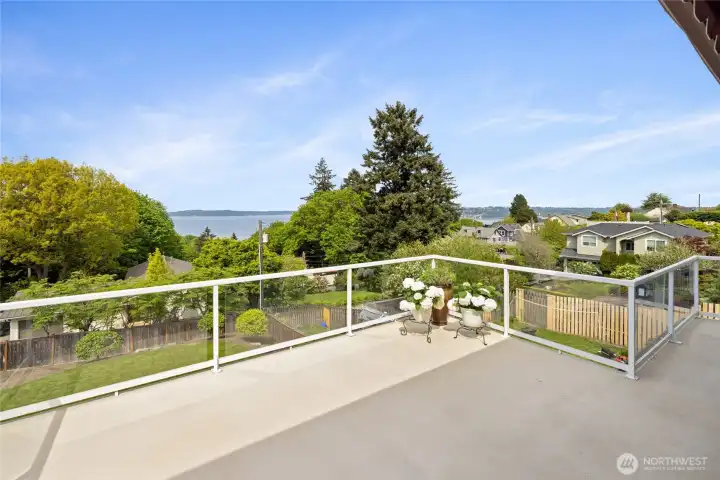 Spacious entertaining deck with sleek glass railing showcases unobstructed water views and lush surroundings—perfect for relaxing or hosting. Panoramic outlook from the deck captures a blend of water views, mature trees, and neighborhood charm, offering a peaceful and scenic setting.
