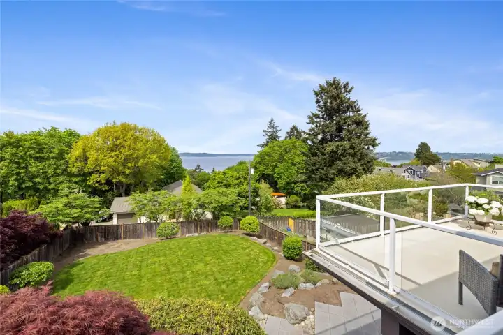 Elevated perspective highlights beautifully landscaped yard below with manicured lawn, terraced plantings, and stunning water backdrop.