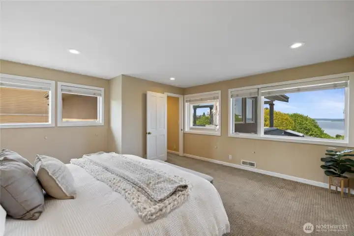 Serene primary suite with expansive windows capturing partial water views and treetop outlooks, creating a calm and light-filled atmosphere.