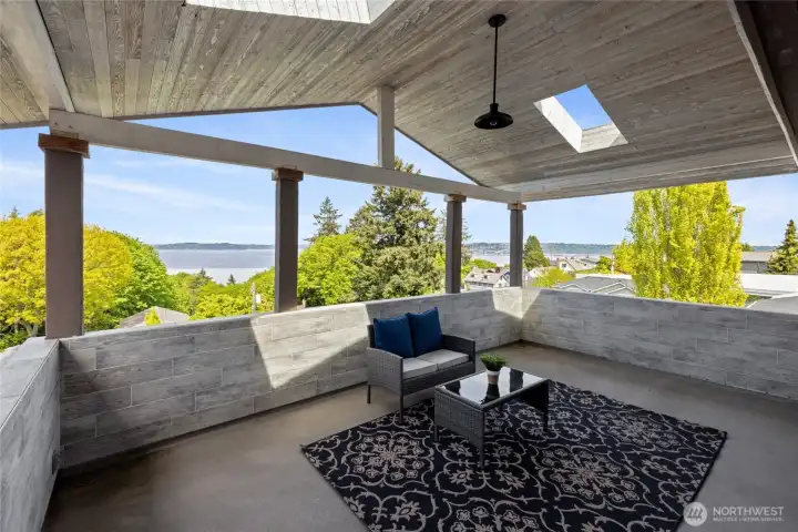 Expansive covered deck off the primary suite featuring vaulted wood ceilings, skylights, and ample space for year-round enjoyment with stunning Sound views. Elevated vantage point offers beautiful views of the Sound framed by mature trees and surrounding landscape—an ideal setting for peaceful mornings or evening sunsets.