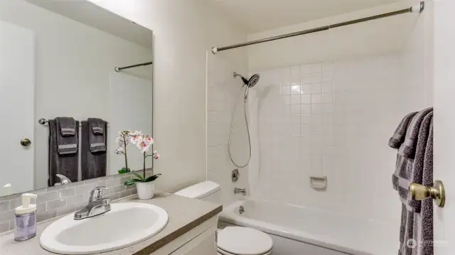 A spacious full guest bathroom upstairs featuring a relaxing shower/tub combo, a large mirror, and crisp white walls.