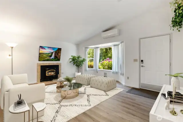 Stylish and serene—this airy living room features a vaulted ceiling, new flooring, inviting fireplace, and large bay window overlooking vibrant landscaping. (Virtually Staged)
