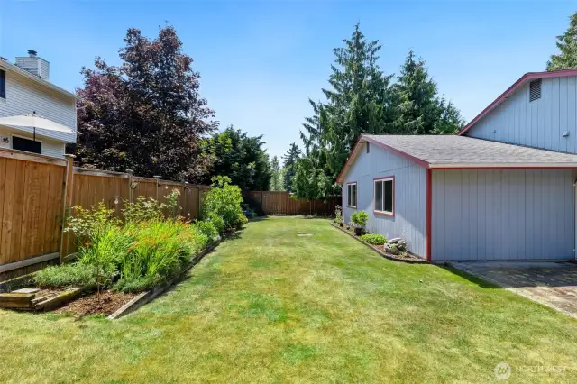The fully fenced yard stretches along the home with curated garden borders, framed by evergreens for added privacy and shade.