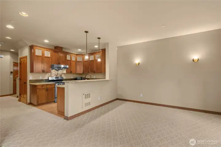 Another view of the great room, showing the breakfast bar and kitchen peninsula that separates the space. The lights in the tall ceilings adds light, while the wall sconces create a cozy atmosphere.