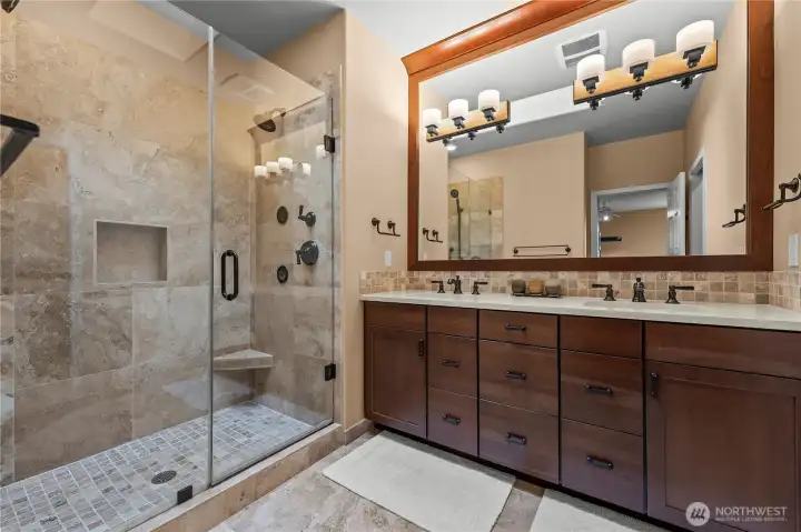 Spa-inspired primary bath with custom cabinetry, granite counters, tile flooring, and walk-in shower with dual shower heads.